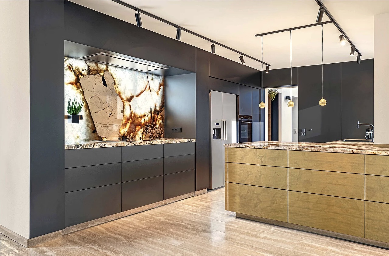 Merton & imi Metal - Et flot mørkeblåt køkken med en stor køkken Ø med fronter i messing fra imi metal serie. Messingen står flot sammen med den mørkeblå og den brunlige marmor bordplade. 