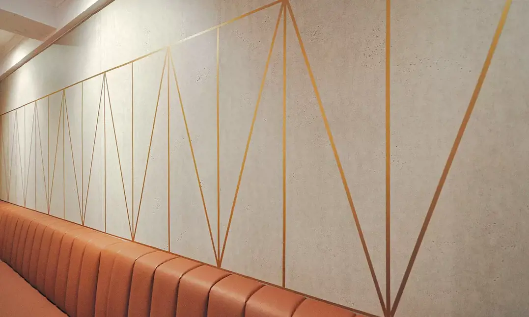Merton & imi Beton - En bagvæg i et flot kreativt trekantsmønster lavet af imi Beton paneler og kobber. Væggen skaber med dens grafiske udtryk og med brug af materialernes flotte kontrast, en dragende baggrund i cafeens lokaler. 