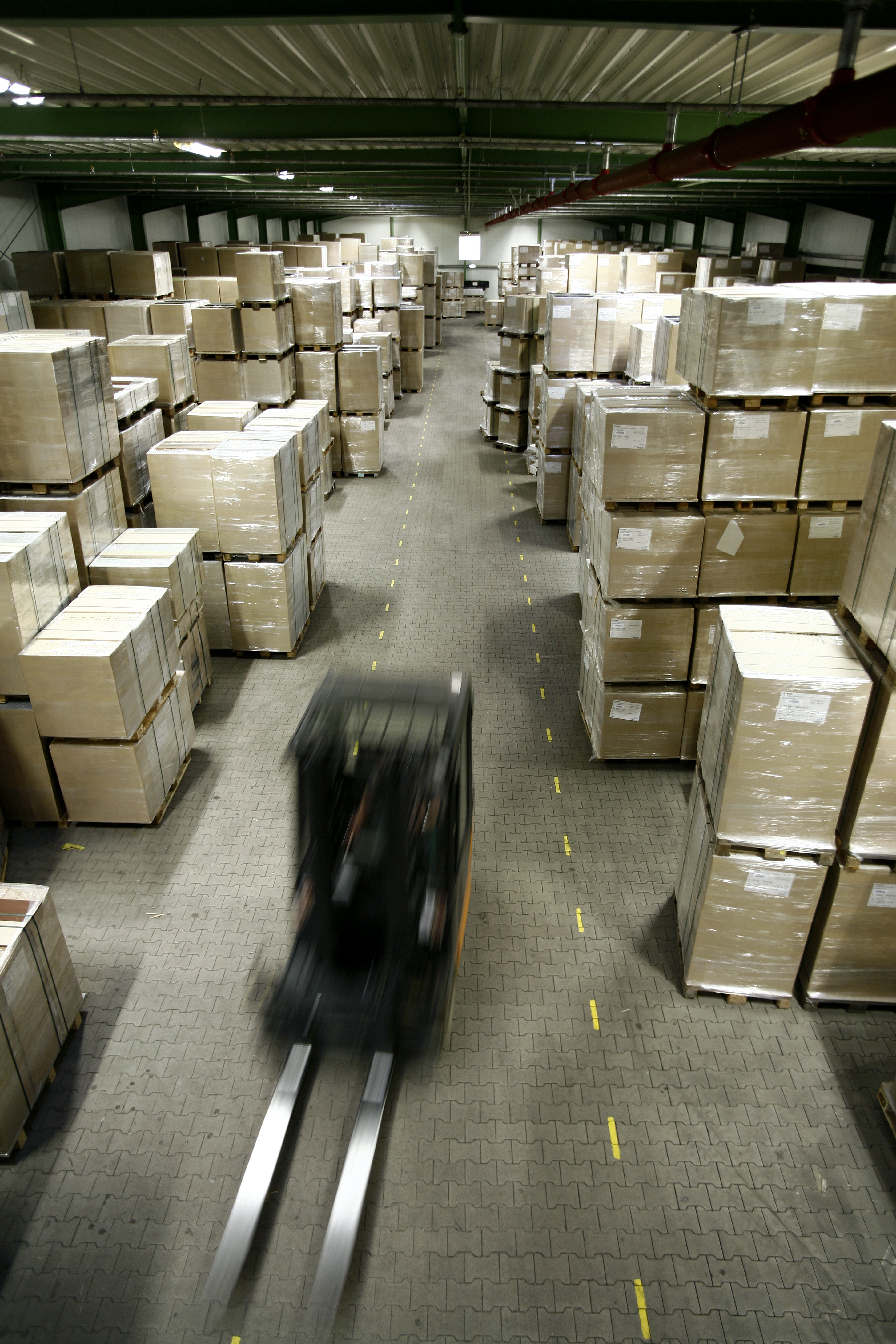 Lagerbillede af en truck i fart og en masse paller med pakkede dele.