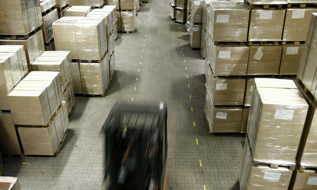 Lagerbillede af en truck i fart og en masse paller med pakkede dele.